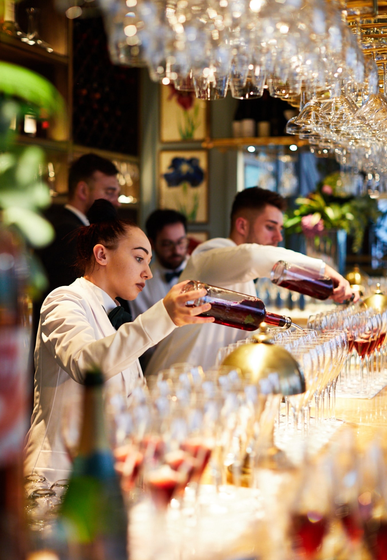 Bartenders fill up a number of lined up glasses.